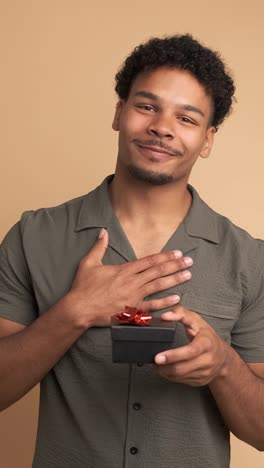happy young man receiving gift box in beige studio