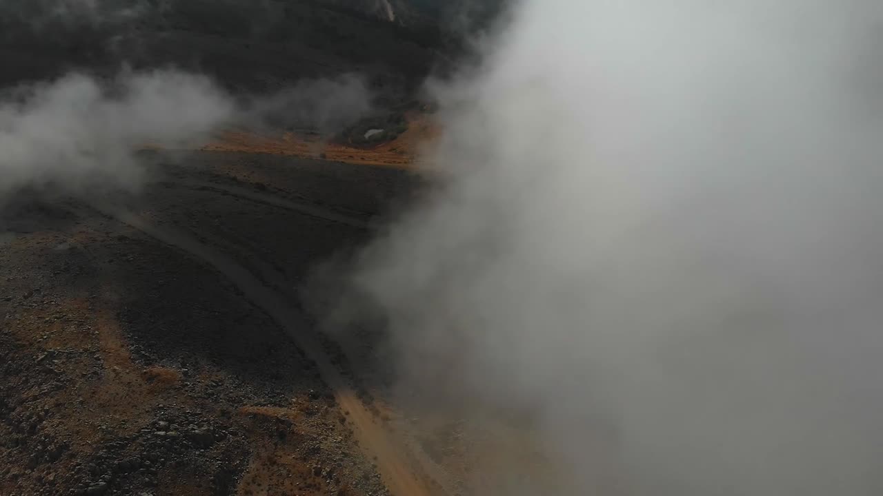 Drone aéreo subindo através de nuvens densas para revelar uma paisagem montanhosa dramática. Movimento atmosférico de névoa e revelação épica da paisagem para temas de viagem e aventura.