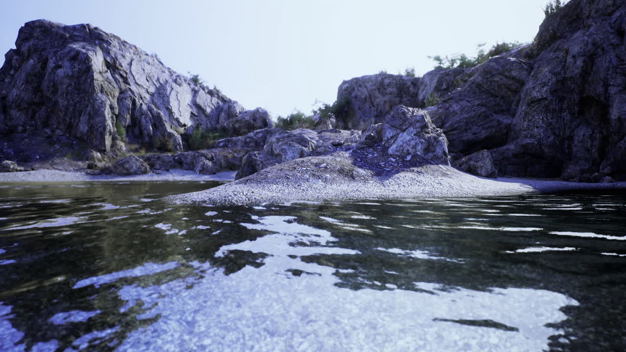 Rocky shoreline with calm water reflecting the clear sky at midday