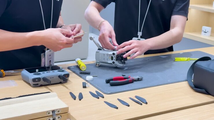 Two technicians assemble drone parts on workbench under bright lighting, using tools and careful coordination