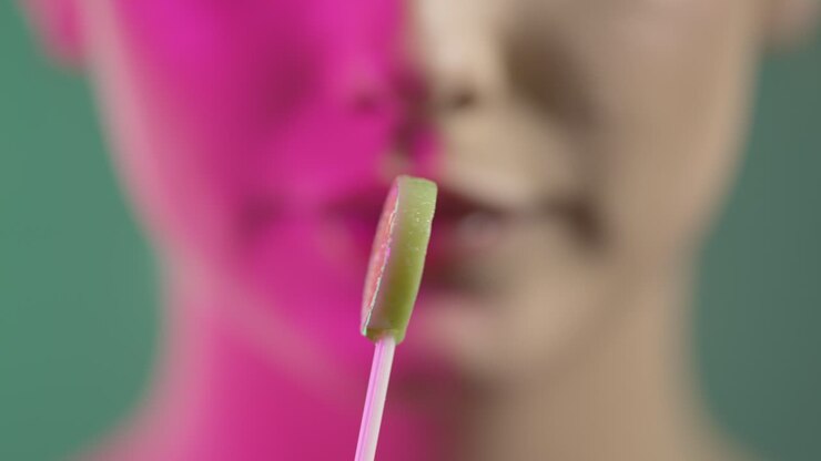 Primo piano del viso di una giovane donna che lecca un lecca-lecca al lime con un sorriso felice.
