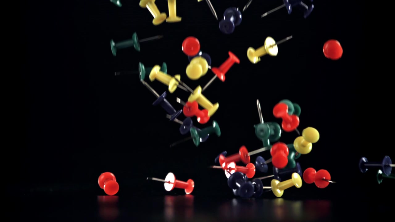 Assorted Colorful Pushpins Falling onto a Black Background in Slow Motion