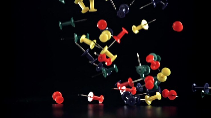 Assorted Colorful Pushpins Falling onto a Black Background in Slow Motion