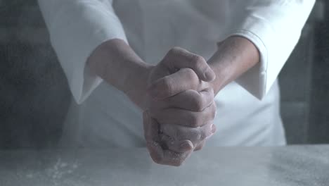 unrecognizable baker chef hands clapping with flour, sprinkling and creating a white cloud of floured powder in the air, slow motion fixed close up shot