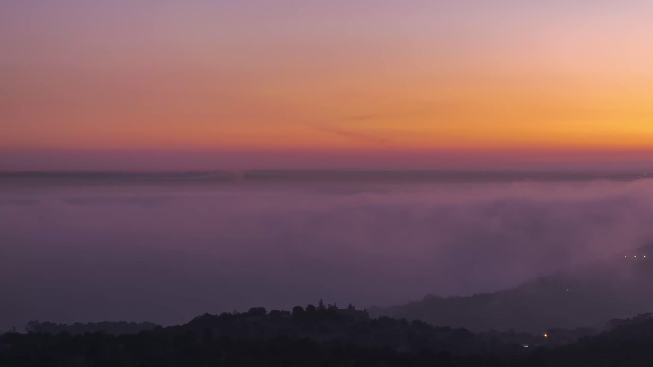 vista aérea de la ciudad moderna y las montañas cubiertas de nubes de garrapatas bajo un cielo colorido durante la puesta del sol