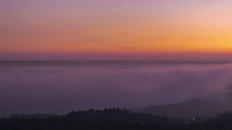 aerial view of modern city and mountains covered with tick clouds under colorful sky during sunset