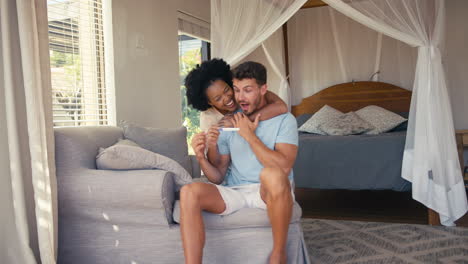 Excited-Couple-In-Bedroom-At-Home-Celebrating-Positive-Pregnancy-Test-Result