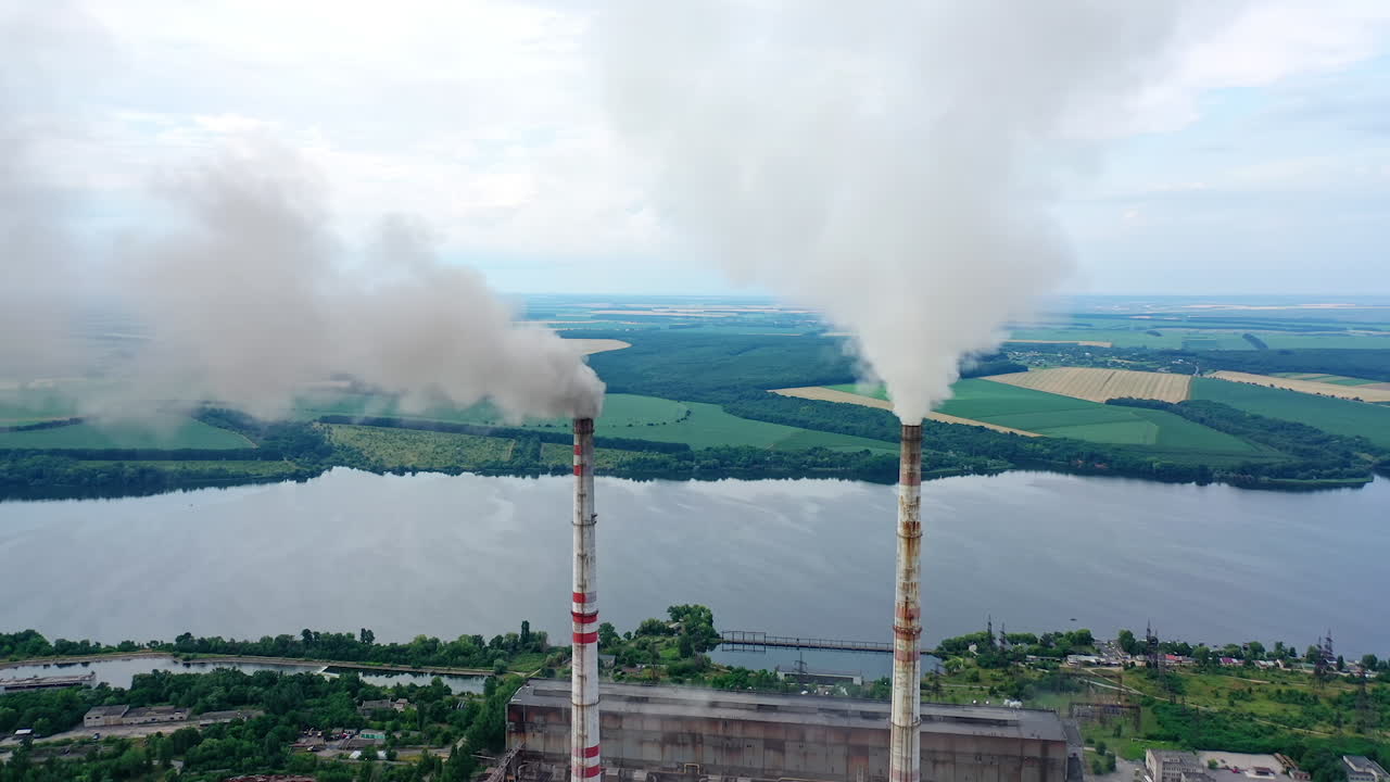 White stack of smoke coming out from large chimneys. Factory chimneys releases harmful emissions into the atmosphere on nature backdrop.Environmental problems.