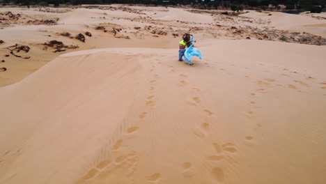 female waving with material on the red sand dunes of mui ne in vietnam dressed in blue with aerial drone footage orbital shot with scenic views of the landscape