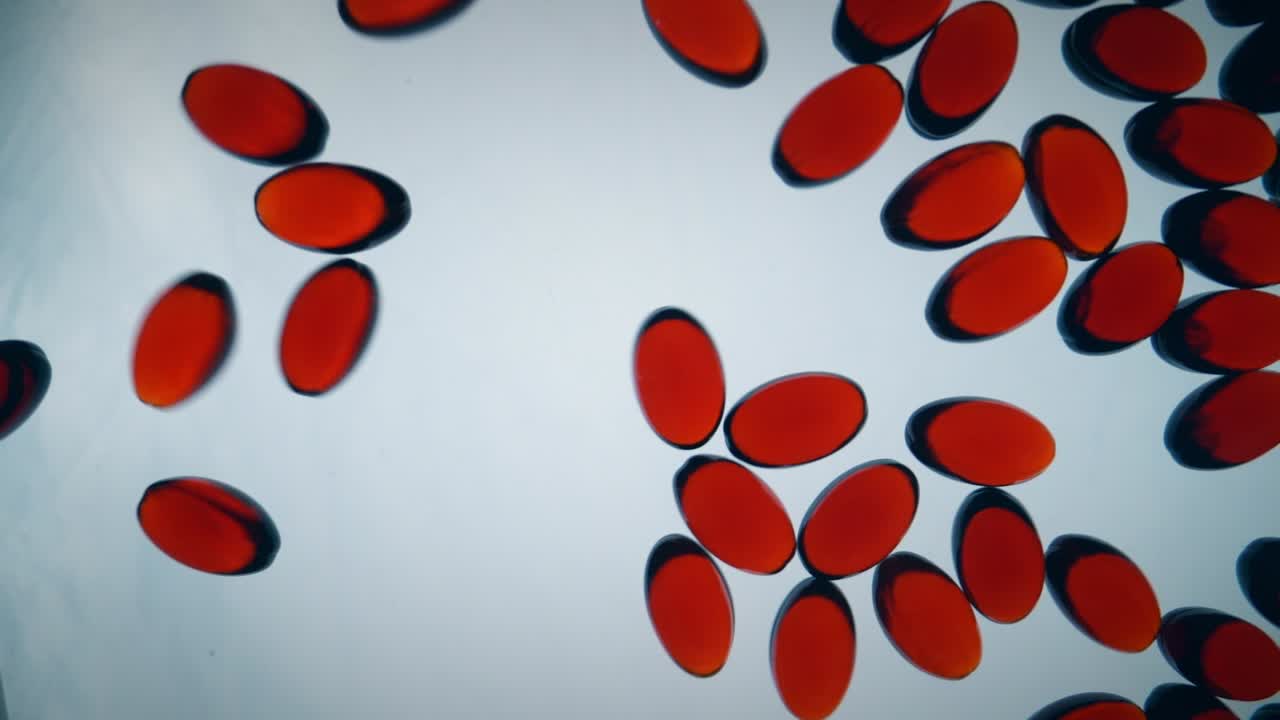 Round red krill oil capsules bouncing over a white surface, slowly filling the frame