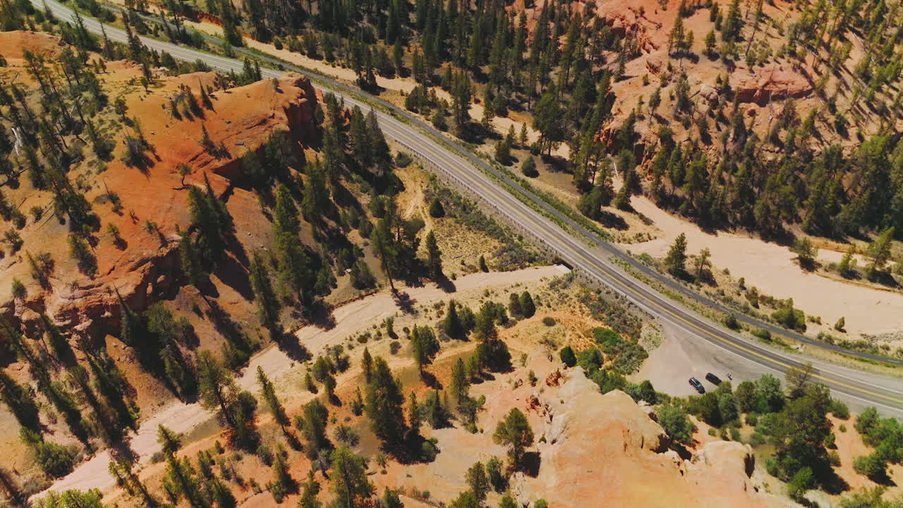 Flying over the orange rocks overgrown with pine trees. Highway passing through the Arches National Park in Utah, USA.