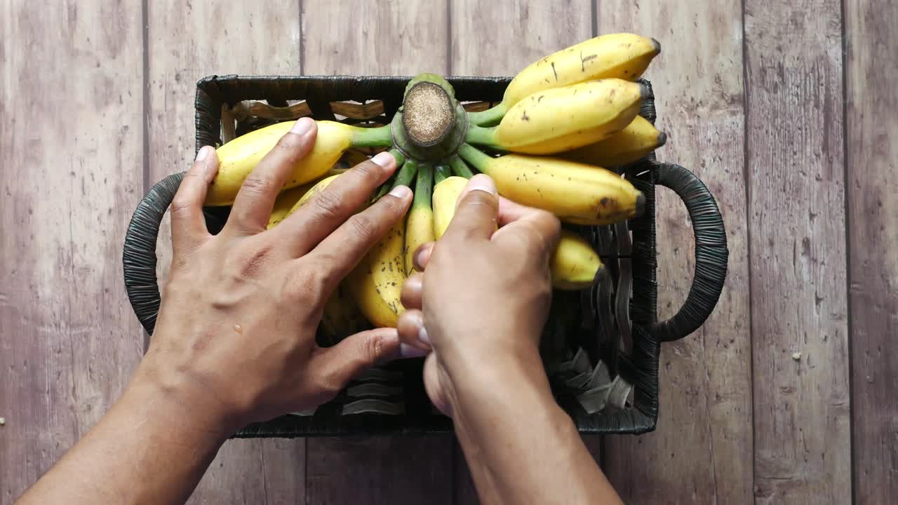manos recogiendo plátanos de una canasta
