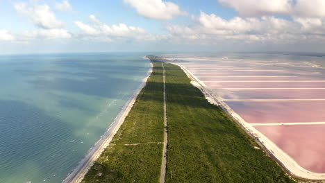 largo camino en el istmo de hierba entre la playa del océano y los estanques de sal rosas