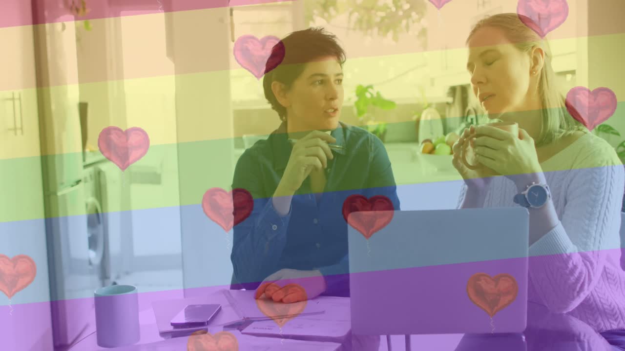 animación de emojis de corazón y bandera del arco iris sobre una pareja de mujeres caucásicas usando una computadora portátil