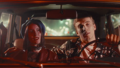 young stylish couple driving through city at night in vintage car