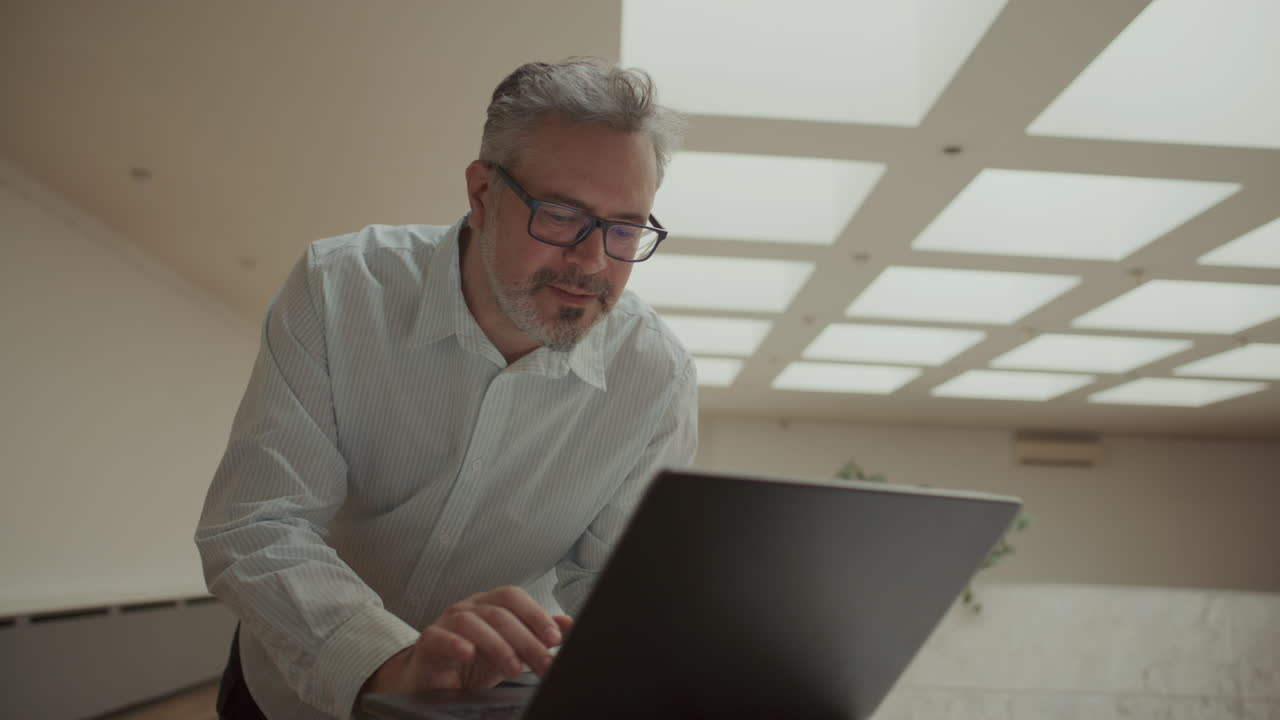 Senior Businessman Browsing the Web on Laptop in Modern Workspace
