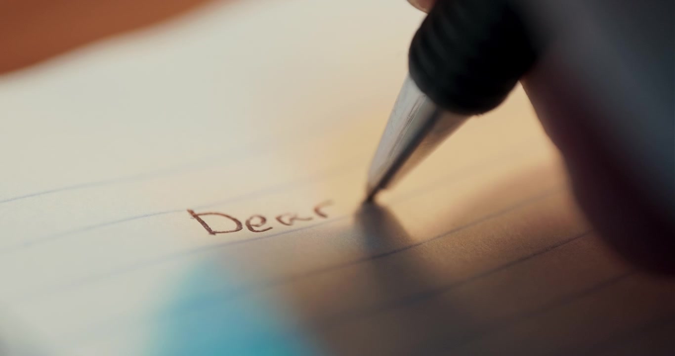 Una macro dettagliata che mostra una penna che scrive le parole "Cara Mamma" su un quaderno bianco, evidenziando il tocco personale di una lettera scritta a mano