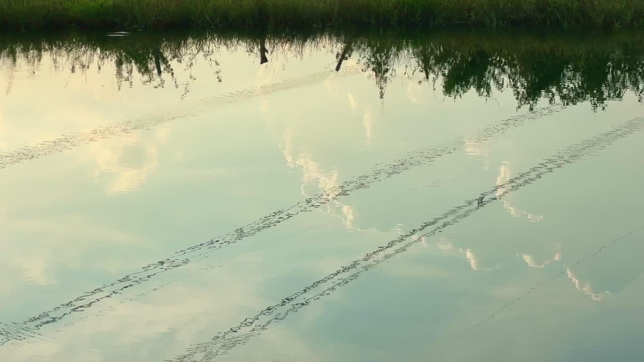 High-voltage transmission lines reflected on a tranquil pond during sunset, merging technology with nature — ideal for educational or documentary use on energy, infrastructure, and environment