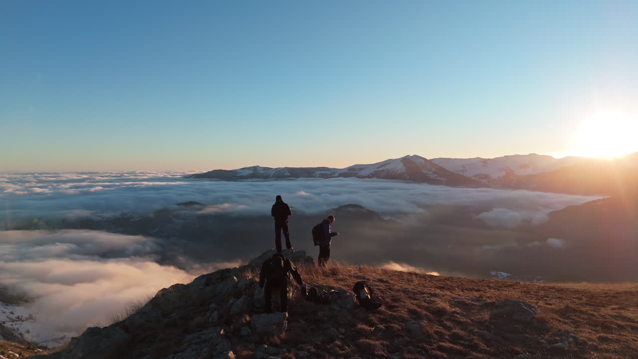 Escursionisti in cima alla montagna con una bellissima alba e nuvole infinite sotto.