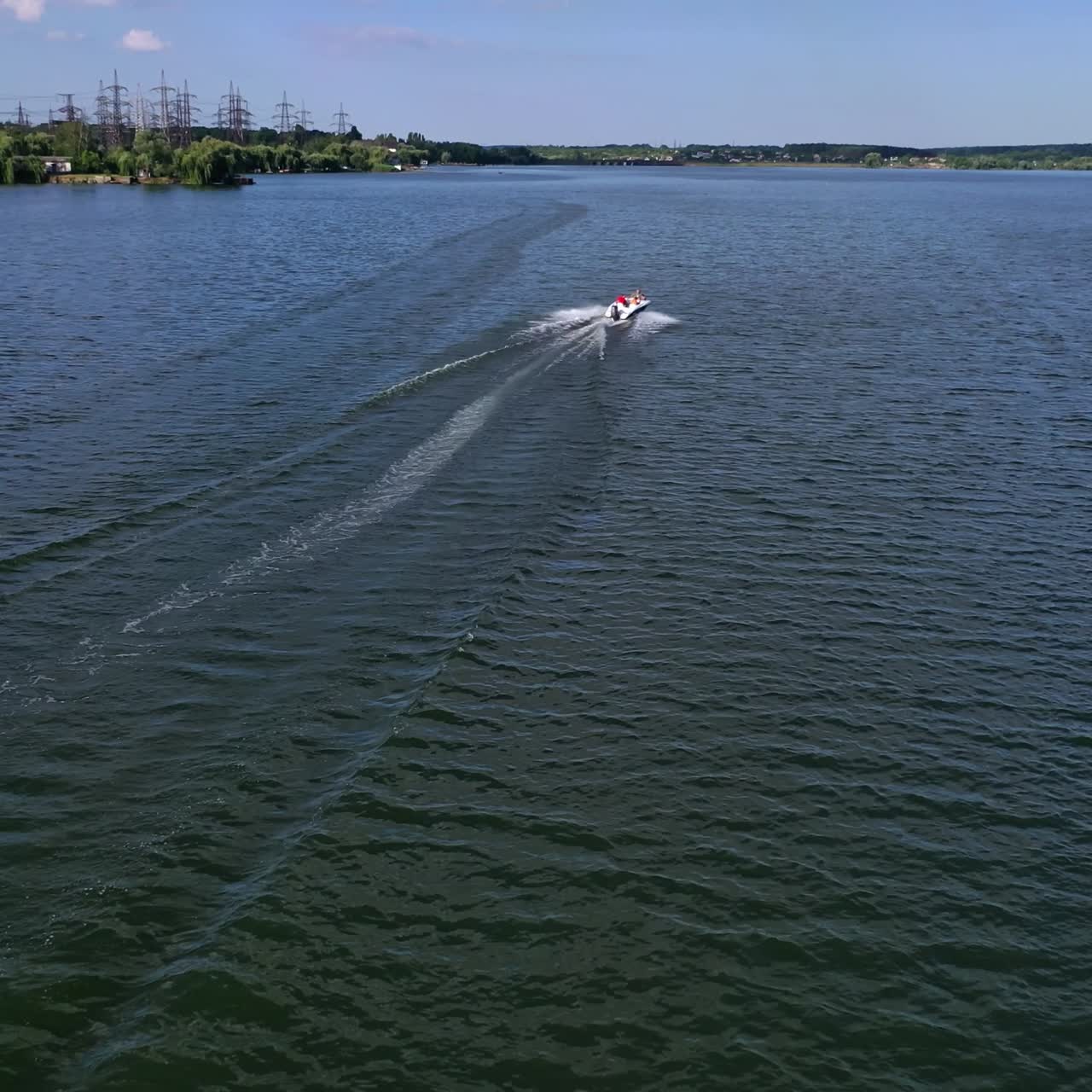 Motor boat on the river. High-speed boat on blue water surface on the background of high-voltage electric lines. Water path after the motion of boat. Aerial view.