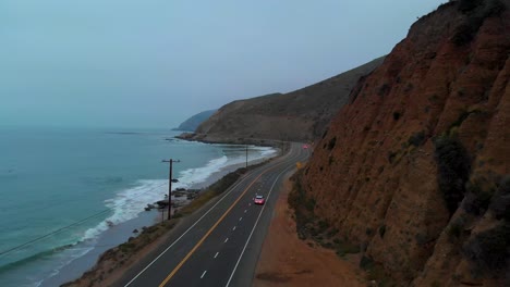 long establishing drone shot following a car as it pulls out onto pacific highway one, near malibu on a grey and foggy morning