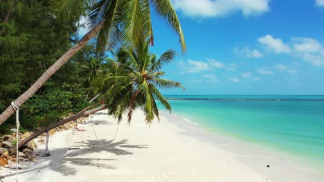 exotic beach with palm trees bent over white sand washed by calm turquoise lagoon under bright sky with white clouds in thailand