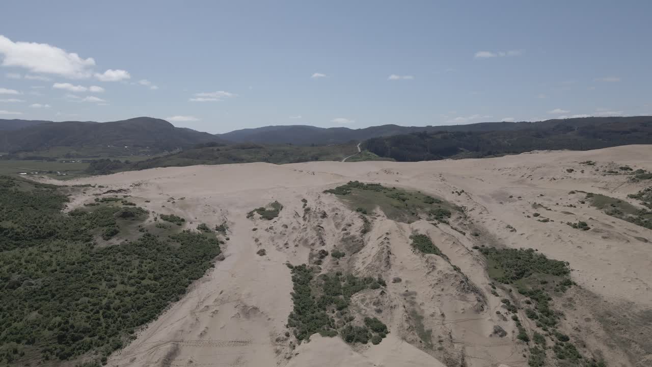 empuje en toma aérea de dunas de arena en llani, chile con arbustos a los lados y montañas en el fondo tomadas durante un día claro y soleado con algunas nubes