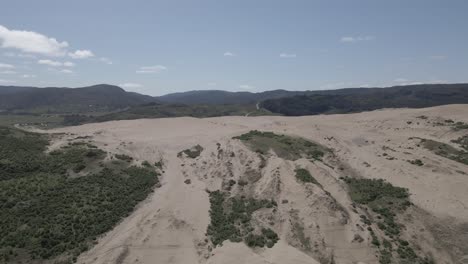 Empuje-En-Toma-Aérea-De-Dunas-De-Arena-En-Llani,-Chile-Con-Arbustos-A-Los-Lados-Y-Montañas-En-El-Fondo-Tomadas-Durante-Un-Día-Claro-Y-Soleado-Con-Algunas-Nubes