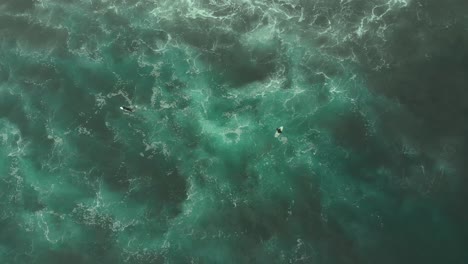 Toma-Aérea-De-Dos-Surfistas-Relajándose-En-Aguas-Turquesas-Desde-Arriba,-Pichilemu,-Chile-4k