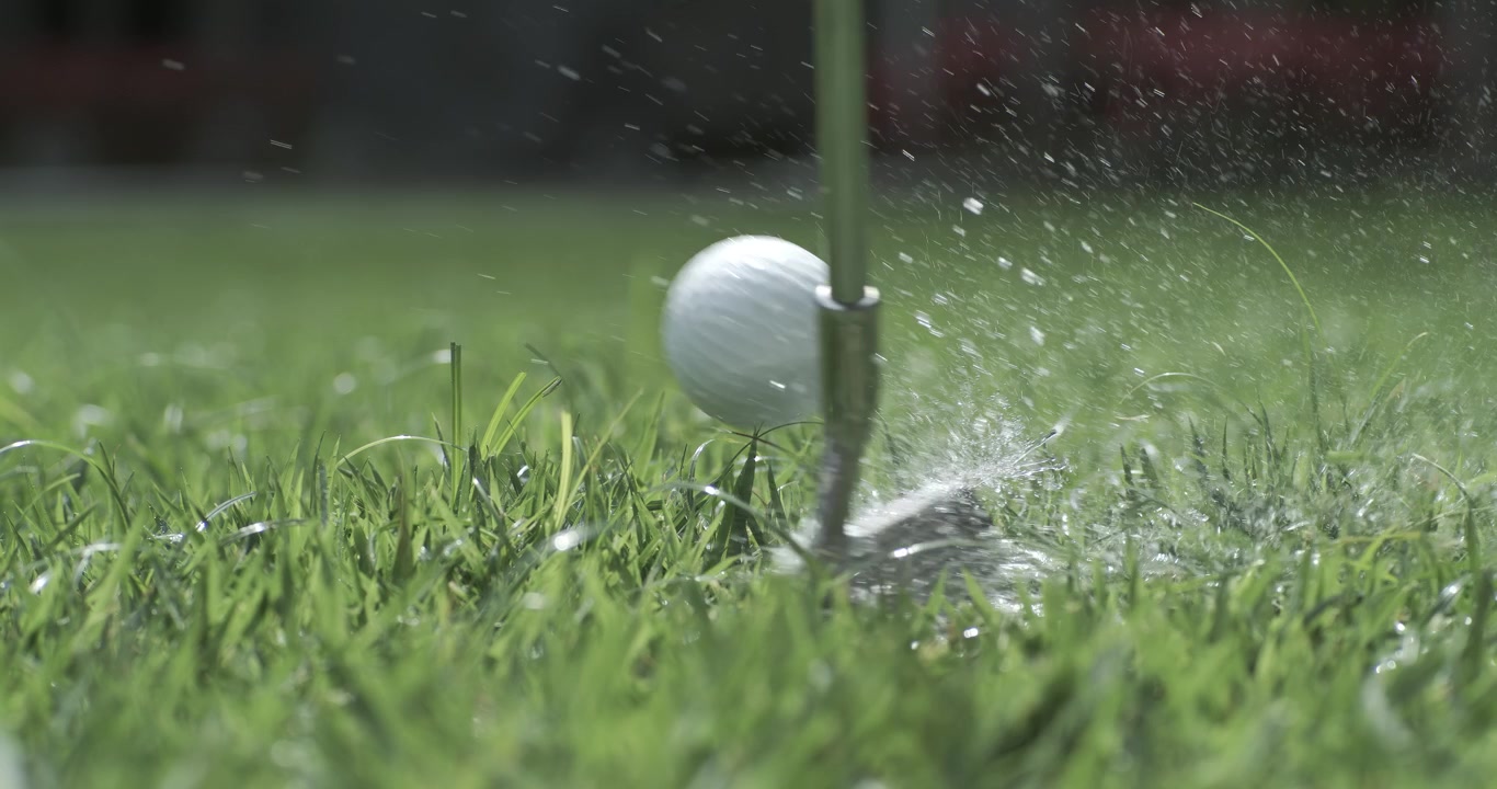 Mazza da golf che colpisce una pallina da golf bianca in super slow motion. Gocce di rugiada mattutina e particelle d'erba si sollevano in aria dopo l'impatto. Ripreso con una telecamera super slow motion a 1000 fps