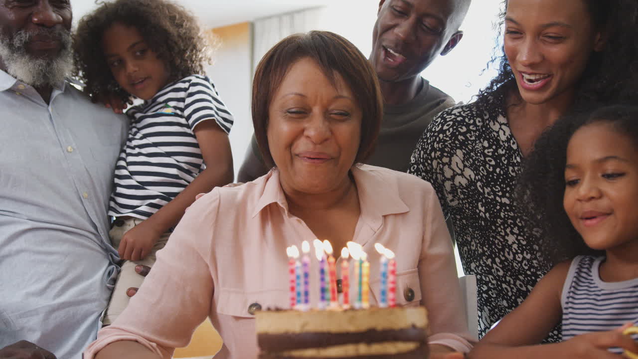 Família multigeracional celebrando o aniversário da avó em casa com bolo e velas.