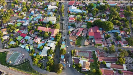 birdseye view of inner city main road with people and vehicles commuting home, colorful tinned roof buildings and tree greenery in dili, timor leste, south east asia, static aerial drone