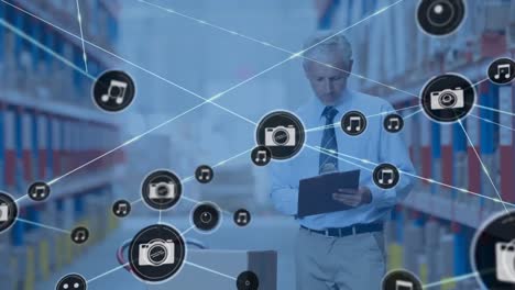 Animation-of-network-of-connections-with-icons-over-man-writing-on-clipboard-in-warehouse