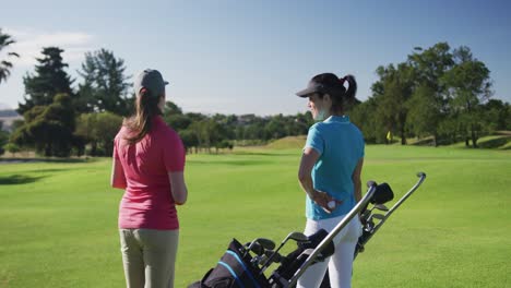 Two-caucasian-female-golf-players-talking-standing-on-golf-field