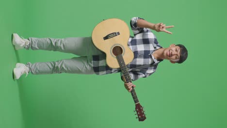 full body of asian teenager with guitar showing gesture peace and smiling on green screen background