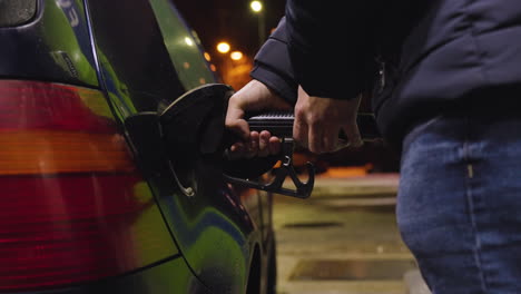 Low-angle-medium-view-of-male-filling-tank-with-gasoline,-excess-drips-off-from-nozzle-at-night