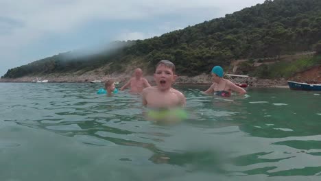 young boy having fun at turquoise beach water, camera follow him imerging and submerging, people in background
