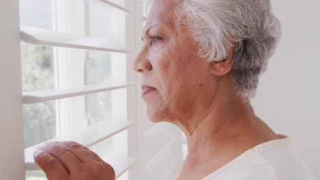 mujer afroamericana mayor mirando por su ventana, en casa