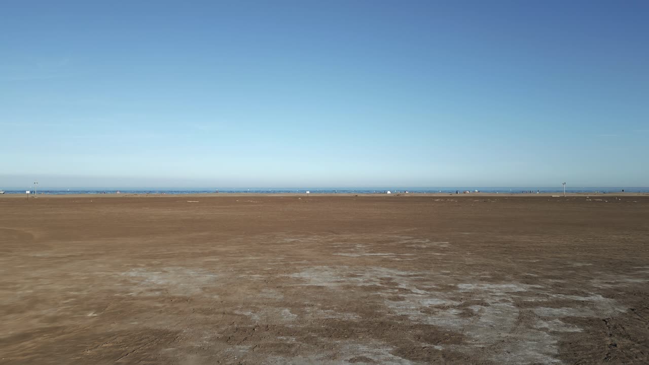 This location features expansive sandy shores, calm waters, and a clear sky. Sailboats can be seen in the distance during a peaceful afternoon at the beach