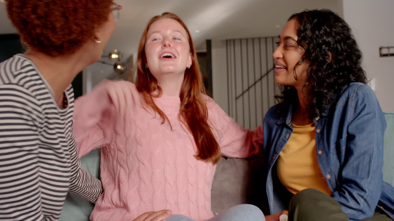 Chatting and laughing, diverse female friends enjoying time together on couch indoors