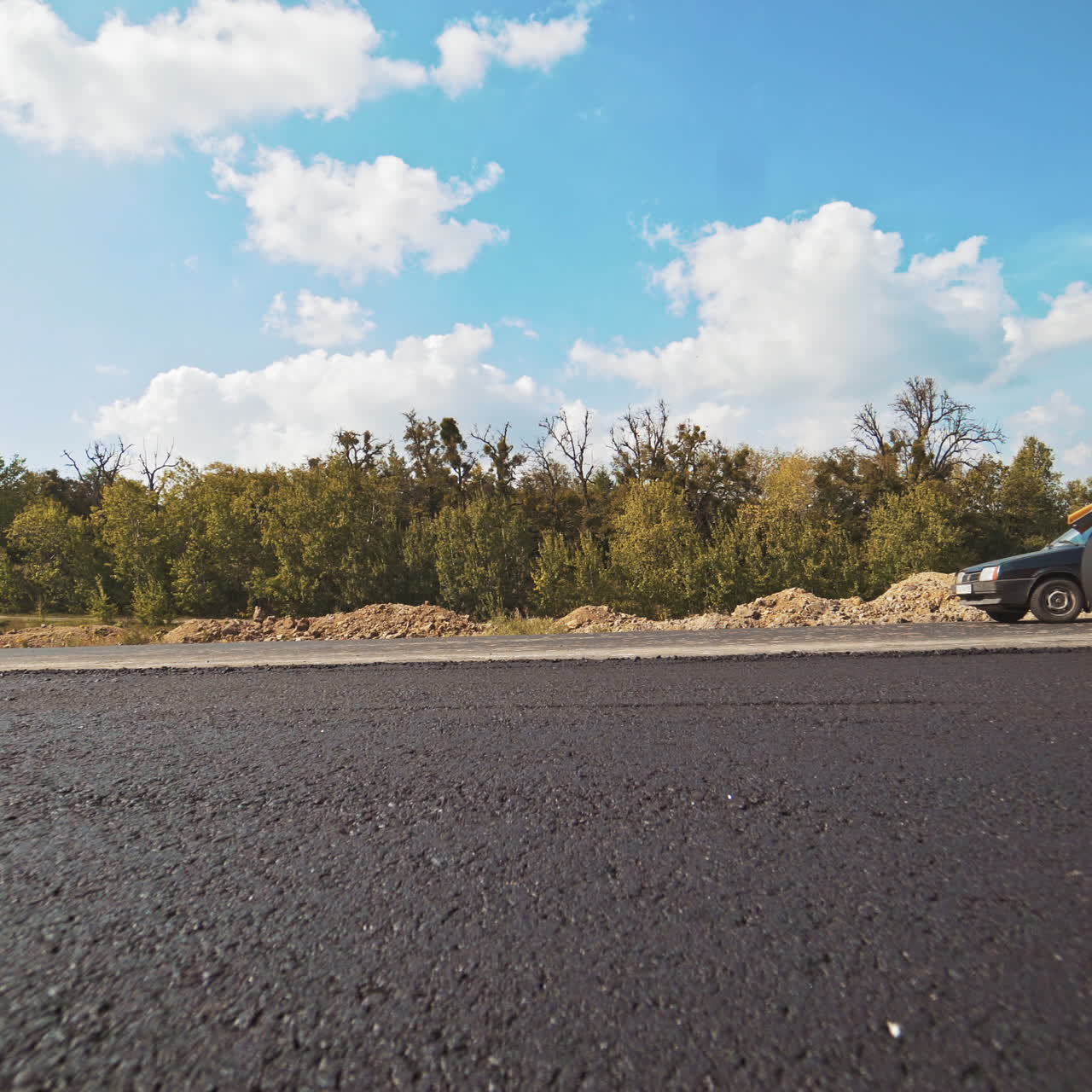 Orange roller machine pressing hot asphalt on the road outdoors. Workers and compactor machine making new asphalt. Street resurfacing.