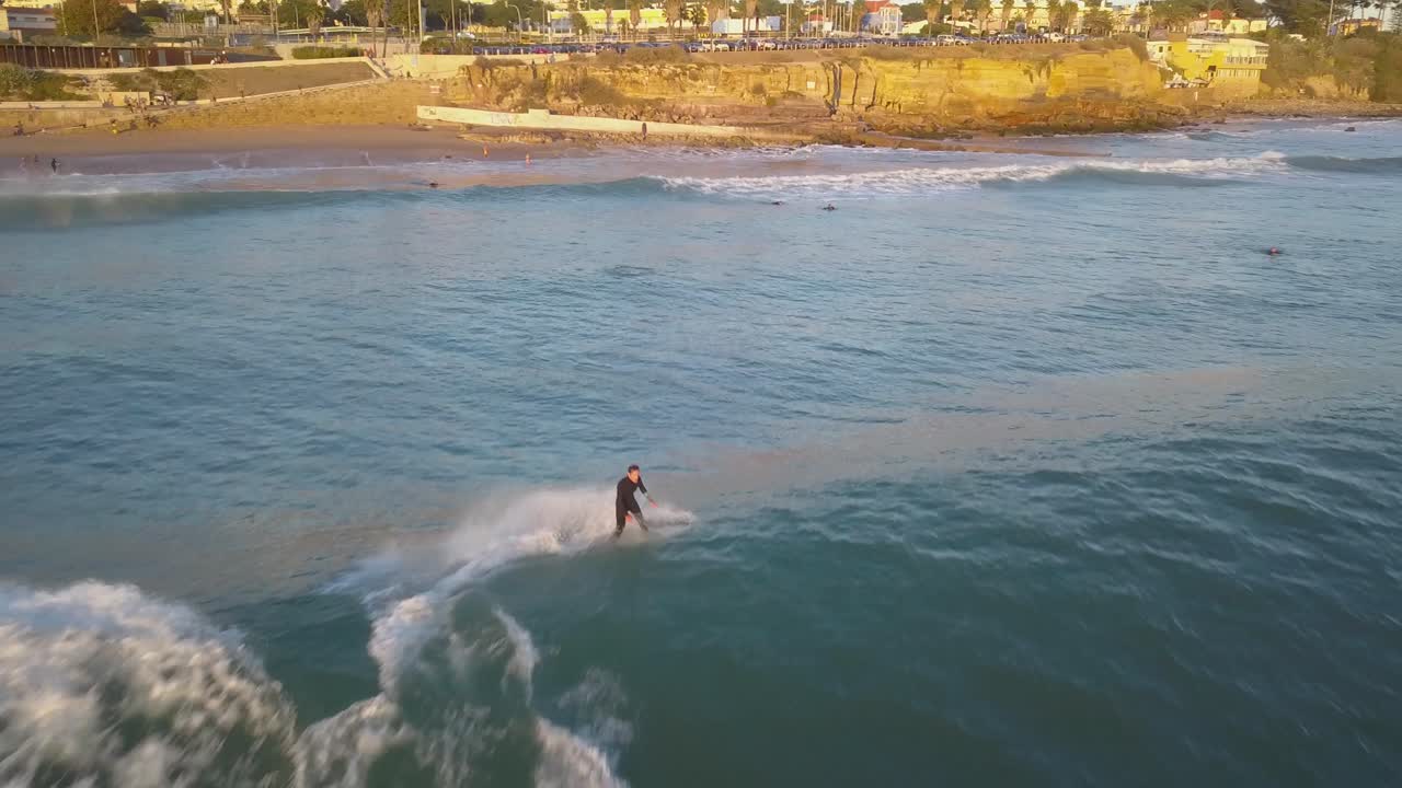 vista aérea siguiendo al hombre surfeando las olas del océano tropical en una tabla de surf en estoril, cascais