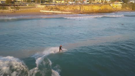 Vista-Aérea-Siguiendo-Al-Hombre-Surfeando-Las-Olas-Del-Océano-Tropical-En-Una-Tabla-De-Surf-En-Estoril,-Cascais