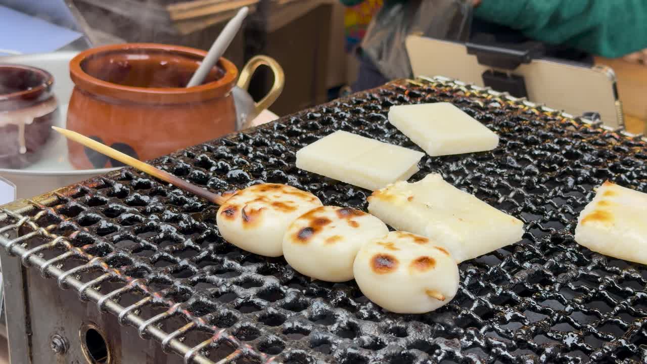 炭火の金網で焼かれている団子串と餅のクローズアップショット。