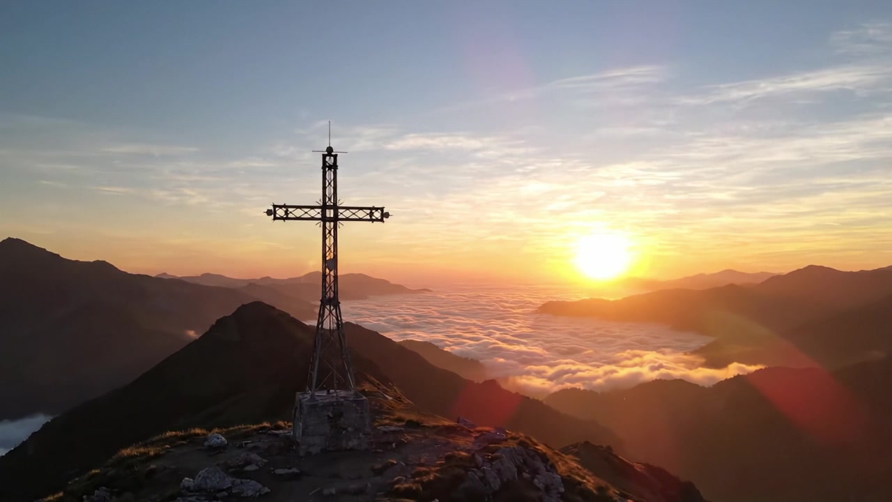 Maestosa alba sulle montagne con una silhouette a croce, catturata da una prospettiva panoramica sopra le nuvole con colori vivaci e bellezza naturale.