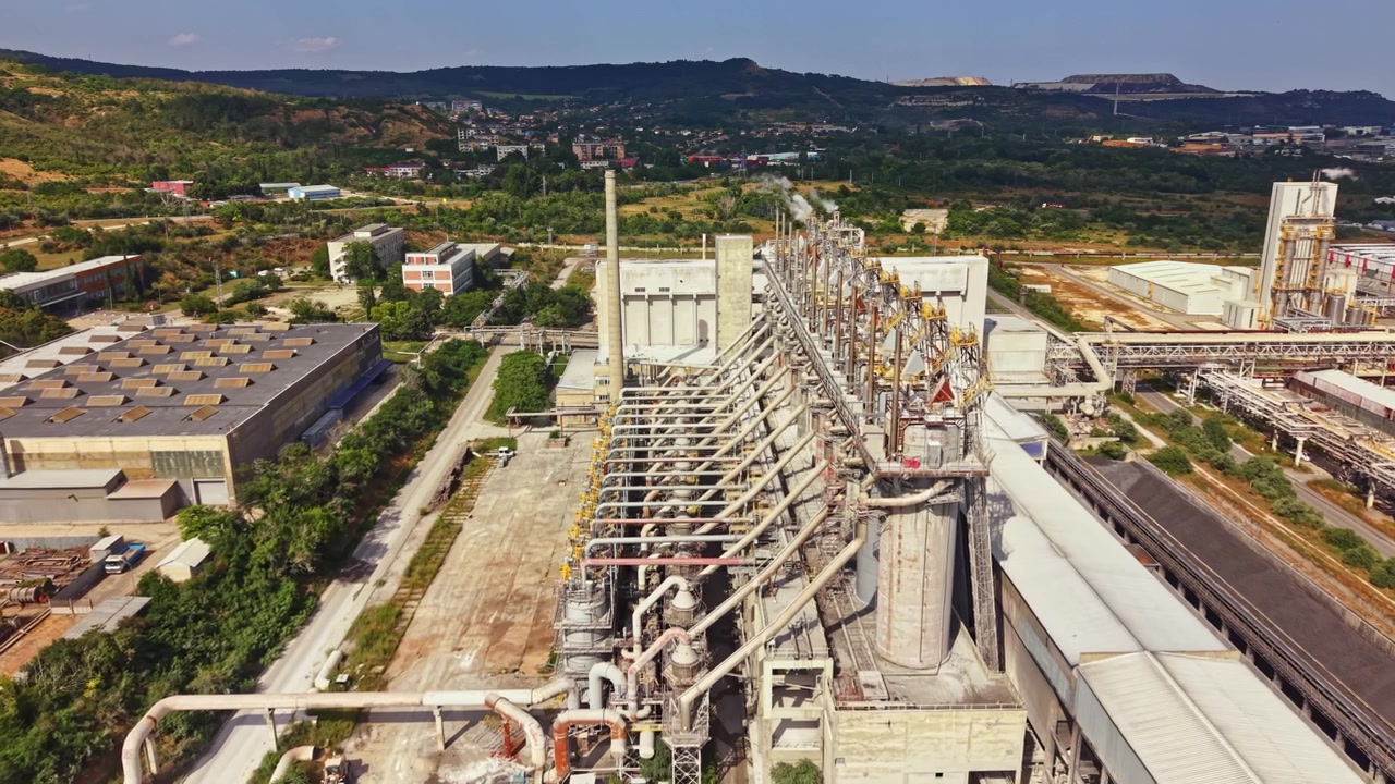 Complesso industriale situato in un'area rurale con varie strutture e attrezzature sotto un cielo azzurro in una giornata luminosa.