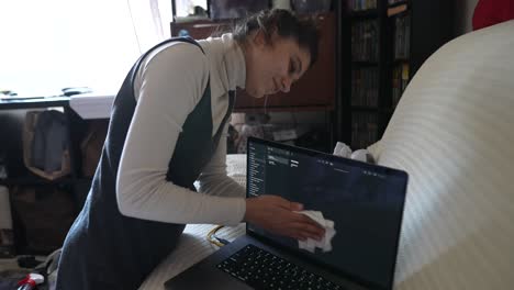 mujer limpiando la pantalla del portátil en casa