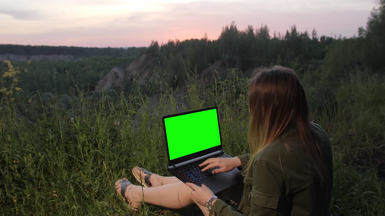 una joven trabajando en una computadora portátil con una pantalla verde en la cima de una montaña.