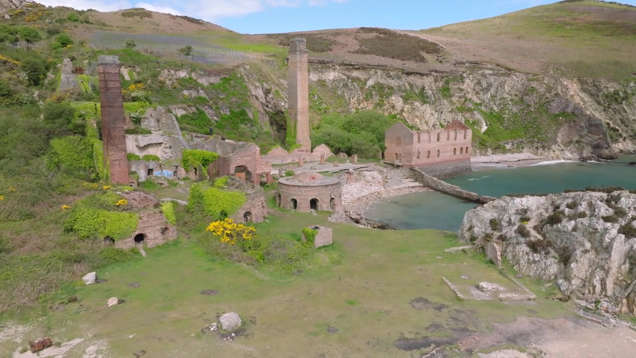 Porth Wen Tuğla Fabrikası, Anglesey, Galler. Terk edilmiş alana doğru yavaş drone yaklaşımı, arı kovanı fırınlarını, aşırı bitki örtüsünü ve bacaları, alan üzerinde hareket eden bulut gölgeleriyle gösteriyor