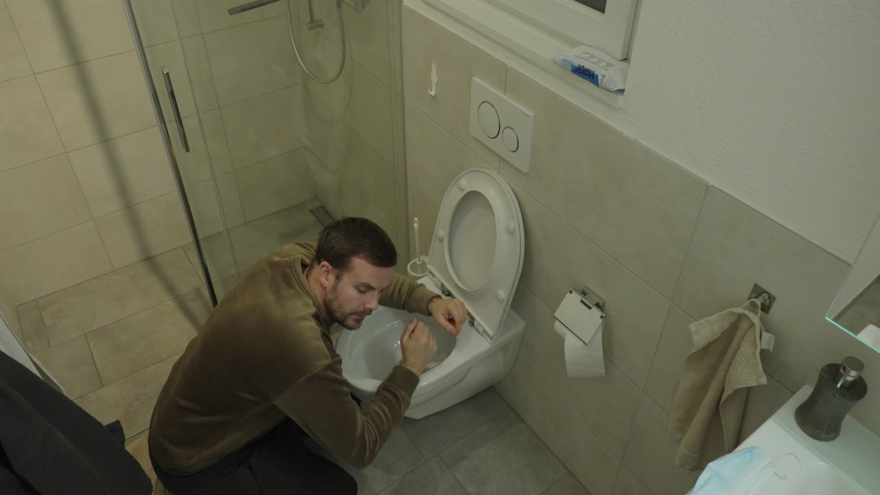 Realistische Top-Down-Szene eines kranken Mannes, der vor einer Toilette kniet und zu Hause Übelkeit und Erbrechen erlebt, symbolisiert Norovirus-Infektion, Lebensmittelvergiftung oder plötzliche Krankheit.